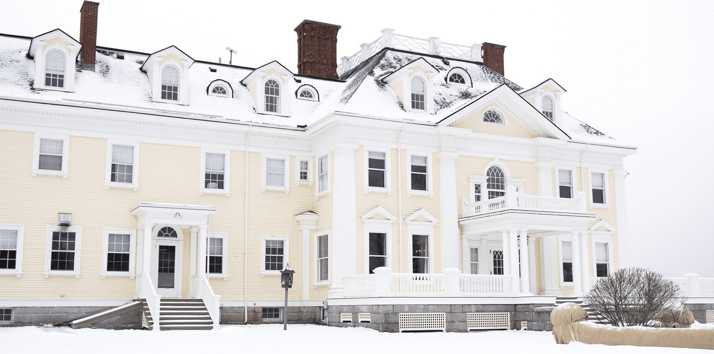 Yellow mansion covered in snow with a white porch.