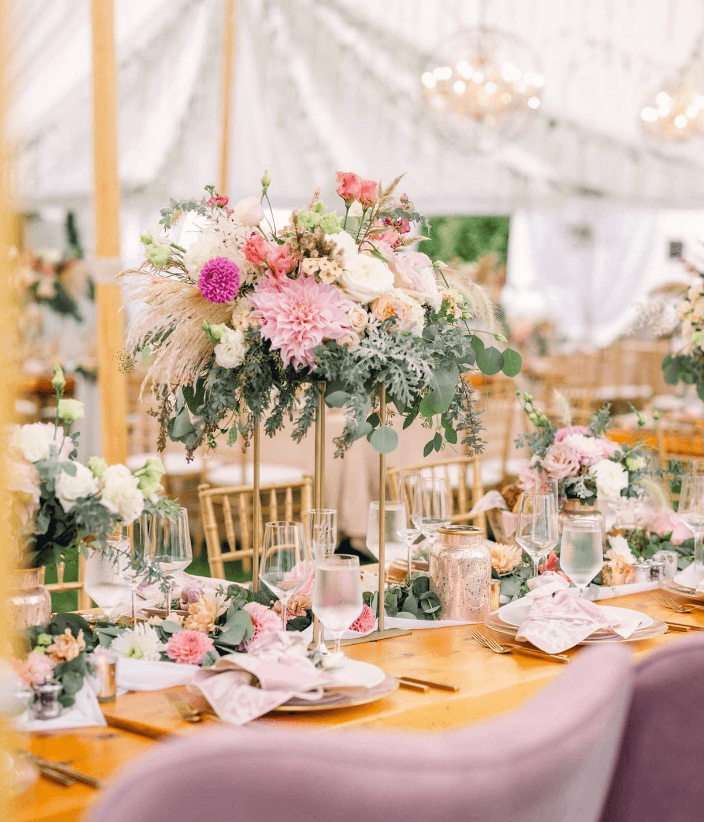 A beautifully arranged table with elegant floral centerpieces under a canopy, set for a special event.