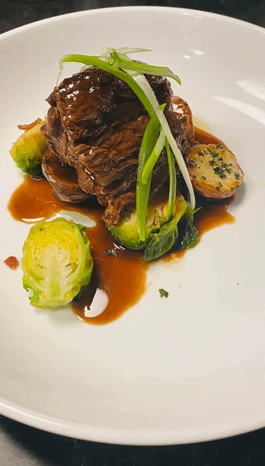 A plated dish featuring tender beef, Brussels sprouts, and a savory sauce garnished with green onions.