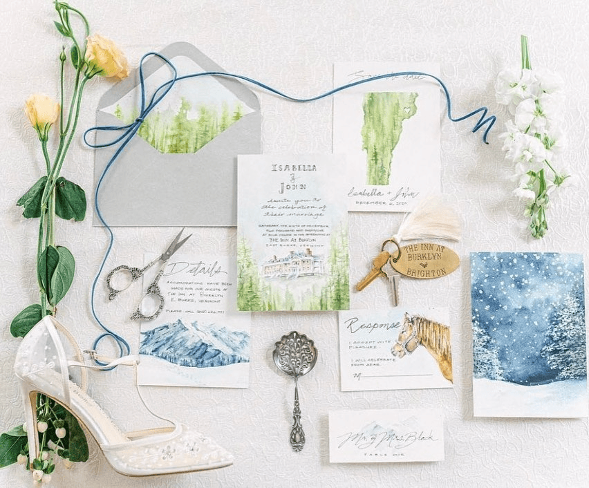 A flat lay of wedding invitations, floral accents, a high-heeled shoe, and decorative elements on a white surface.