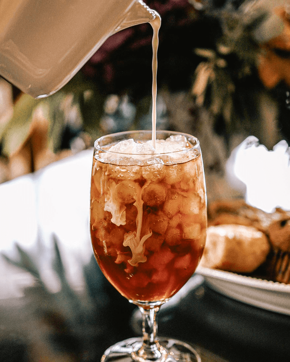 A glass of iced tea with milk being poured over it.