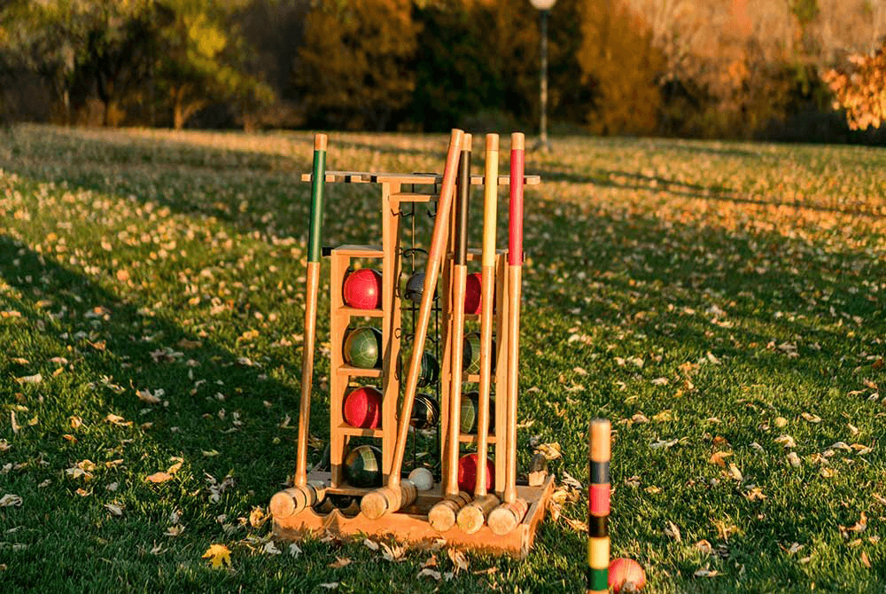 A set of colorful wooden croquet balls and mallets arranged on a grassy field with fallen leaves.