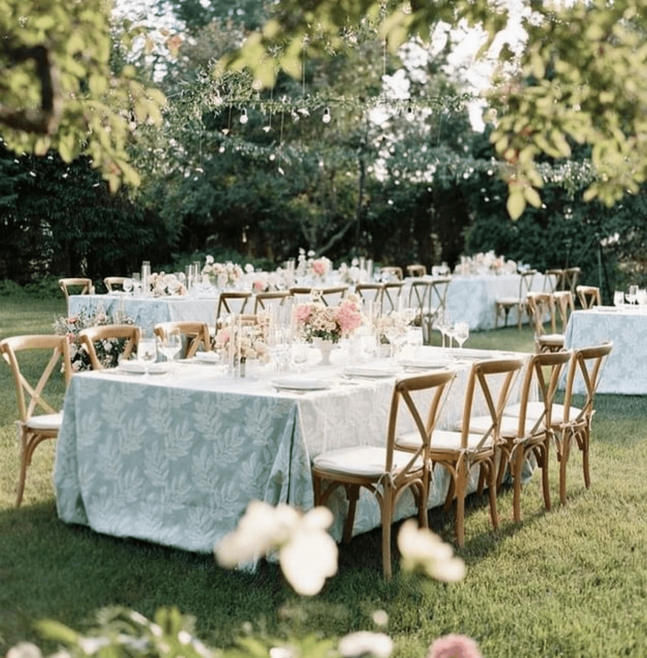 An elegantly set outdoor dining area with tables draped in floral tablecloths and adorned with fresh flowers.